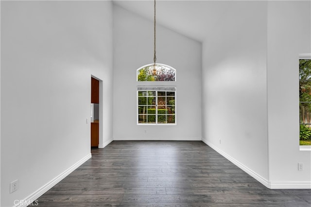 unfurnished dining area featuring high vaulted ceiling, a notable chandelier, dark wood-style floors, and baseboards