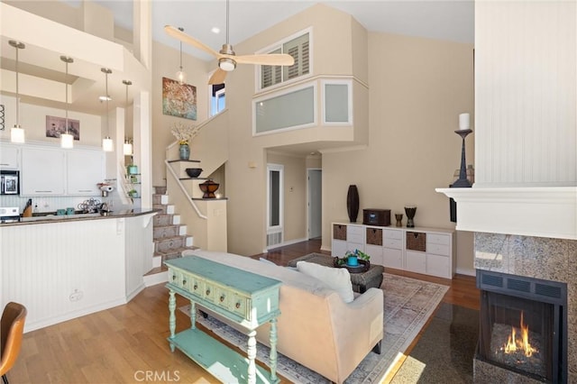 living room with ceiling fan, a lit fireplace, wood finished floors, and a high ceiling