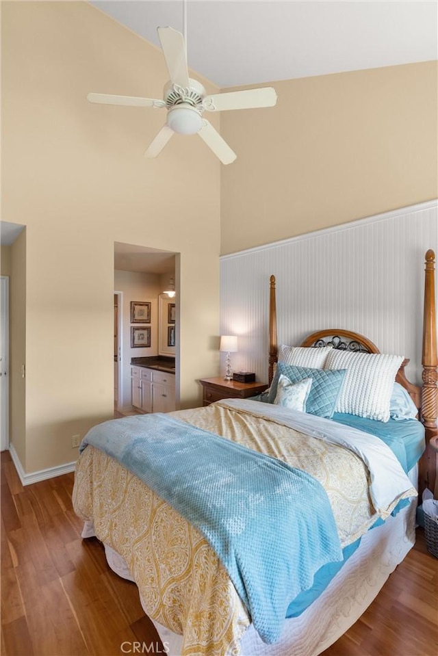 bedroom with ceiling fan, baseboards, high vaulted ceiling, and wood finished floors