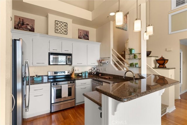 kitchen featuring a peninsula, dark wood-style flooring, a kitchen bar, white cabinets, and appliances with stainless steel finishes