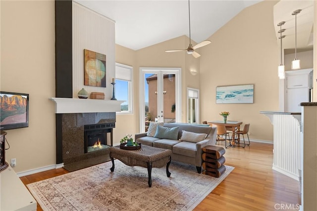 living area featuring a fireplace, light wood-type flooring, baseboards, and a ceiling fan