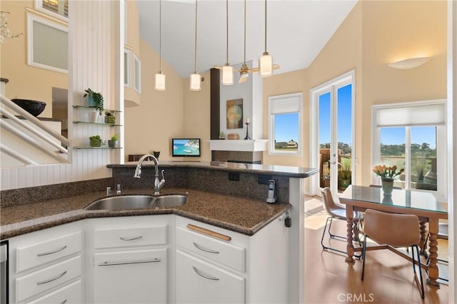kitchen featuring hanging light fixtures, a sink, white cabinetry, a peninsula, and dark stone countertops
