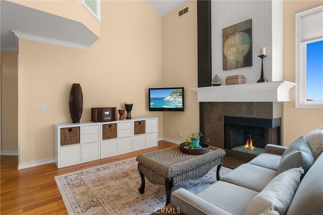 living room with a warm lit fireplace, light wood finished floors, baseboards, and visible vents