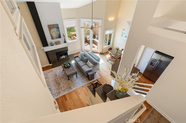 living room featuring a warm lit fireplace, a notable chandelier, a high ceiling, and wood finished floors