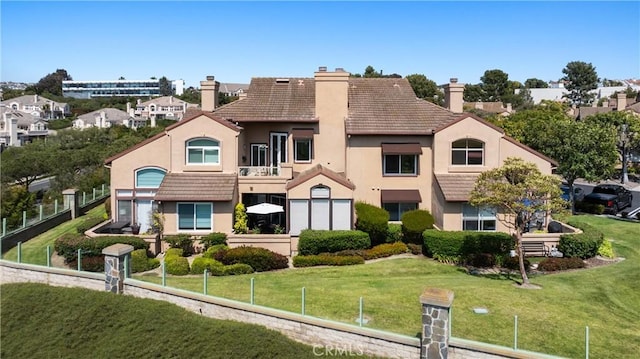 view of front of property featuring a tiled roof, stucco siding, a chimney, a front yard, and fence private yard