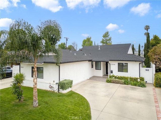 ranch-style home with roof with shingles, fence, concrete driveway, stucco siding, and a front yard