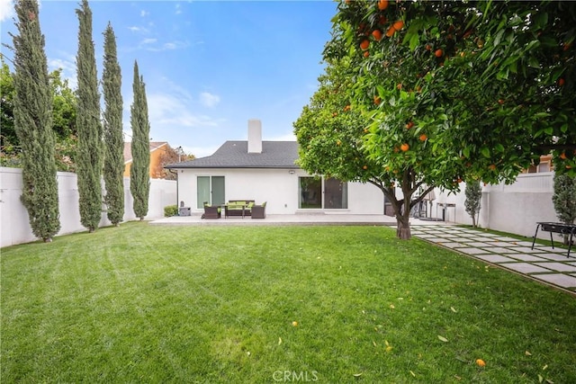 rear view of property with stucco siding, a chimney, a lawn, a fenced backyard, and a patio area