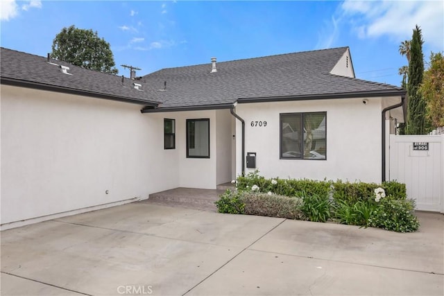 view of front of property with stucco siding, roof with shingles, fence, and a patio