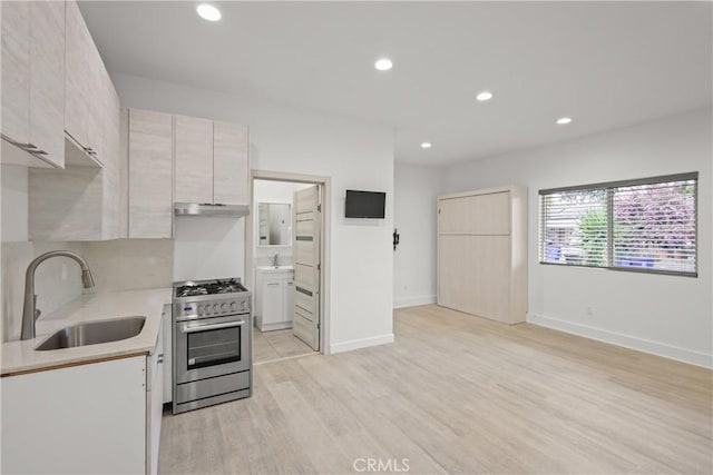 kitchen with recessed lighting, under cabinet range hood, stainless steel range, a sink, and light countertops