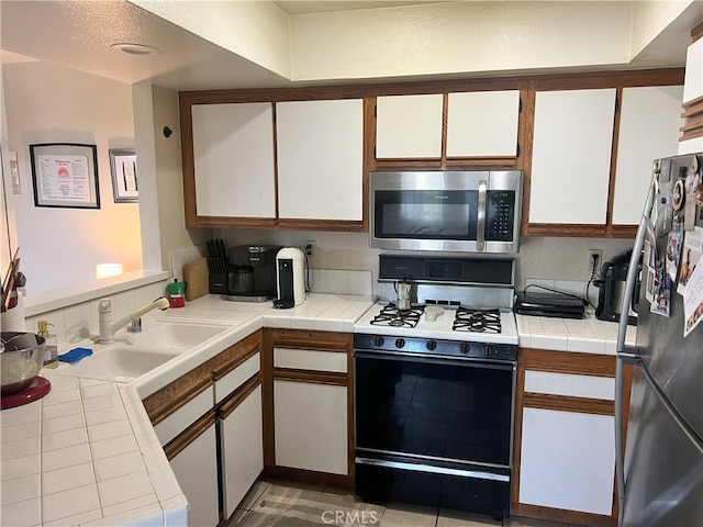 kitchen featuring white cabinetry, tile counters, appliances with stainless steel finishes, and a sink