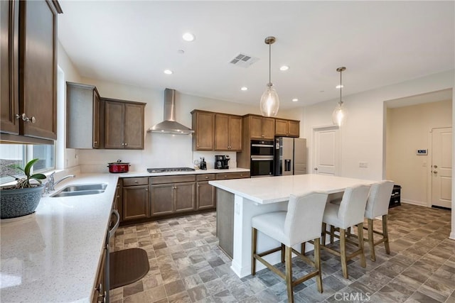 kitchen featuring a sink, a breakfast bar area, wall chimney exhaust hood, visible vents, and appliances with stainless steel finishes