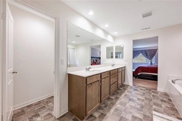 ensuite bathroom featuring double vanity, baseboards, recessed lighting, a walk in closet, and a tub