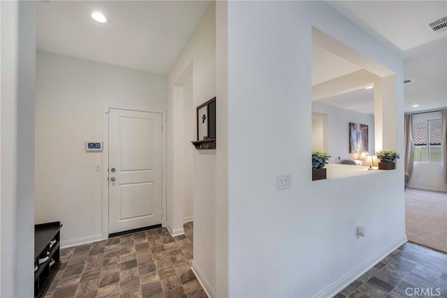 hallway with visible vents, baseboards, and stone finish floor