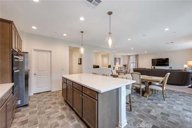 kitchen featuring a breakfast bar, open floor plan, visible vents, light countertops, and a kitchen island