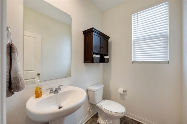 bathroom featuring a sink, baseboards, toilet, and healthy amount of natural light