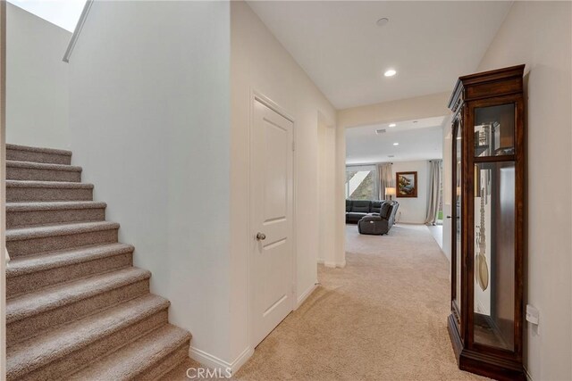 hall featuring baseboards, stairs, recessed lighting, and light colored carpet