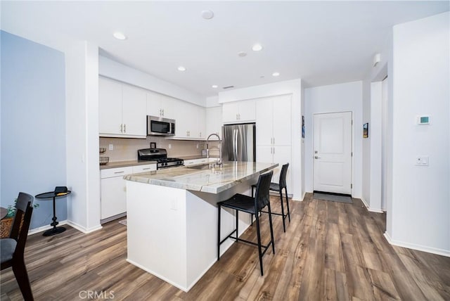 kitchen with a sink, stainless steel appliances, a breakfast bar, a kitchen island with sink, and dark wood-style flooring