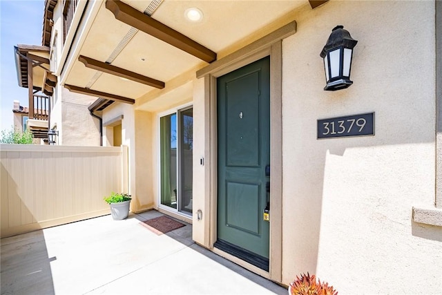 property entrance with stucco siding and fence
