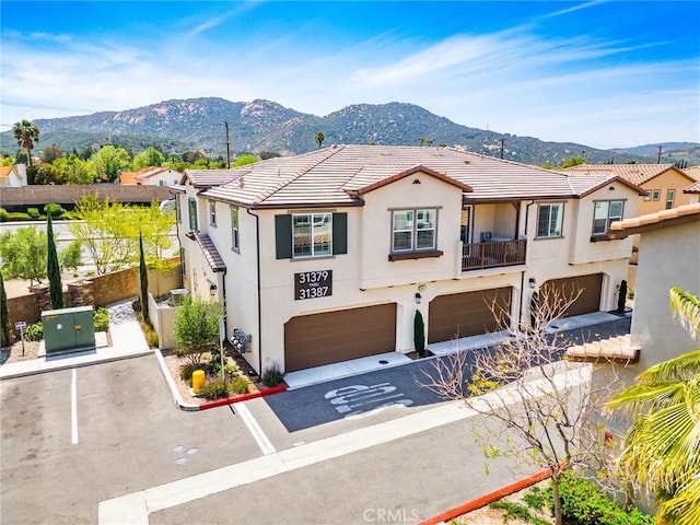 mediterranean / spanish home featuring fence, an attached garage, a mountain view, stucco siding, and a tiled roof