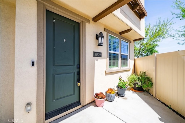 property entrance featuring fence, stucco siding, and a patio area