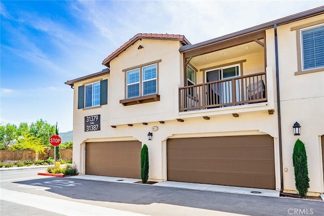view of front of house featuring stucco siding, a garage, and a balcony