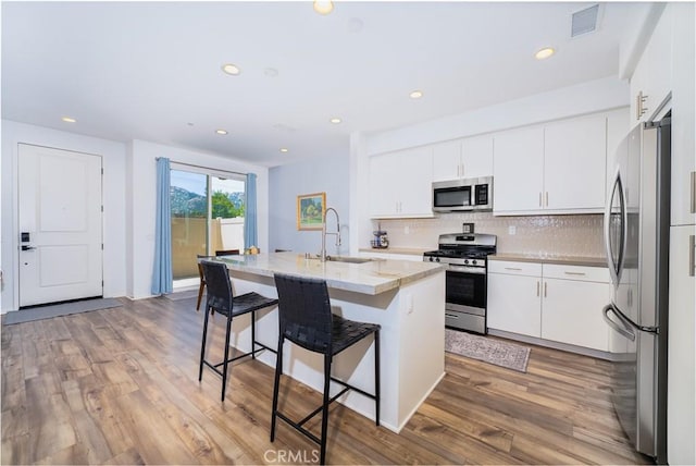 kitchen with a sink, a breakfast bar area, light wood finished floors, decorative backsplash, and appliances with stainless steel finishes