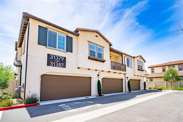 view of front of house featuring fence, an attached garage, stucco siding, and a balcony