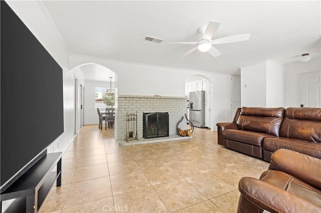 living room with light tile patterned floors, a ceiling fan, crown molding, visible vents, and arched walkways