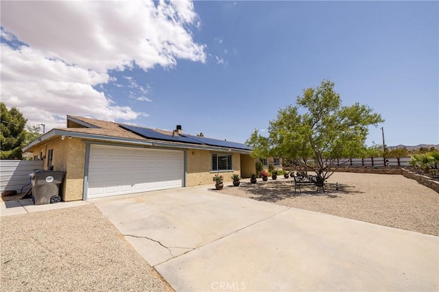 ranch-style home featuring fence, an attached garage, concrete driveway, stucco siding, and solar panels