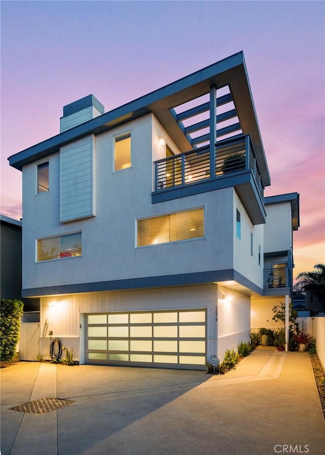 modern home featuring driveway, an attached garage, stucco siding, and a balcony