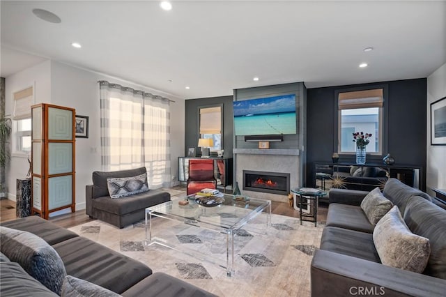 living room with wood finished floors, baseboards, a glass covered fireplace, and recessed lighting