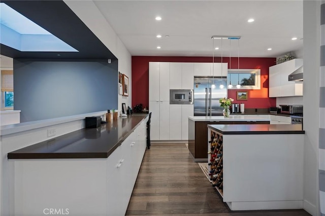 kitchen featuring built in appliances, dark wood finished floors, dark countertops, and white cabinets