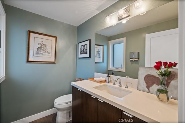 bathroom featuring vanity, wood finished floors, baseboards, and toilet