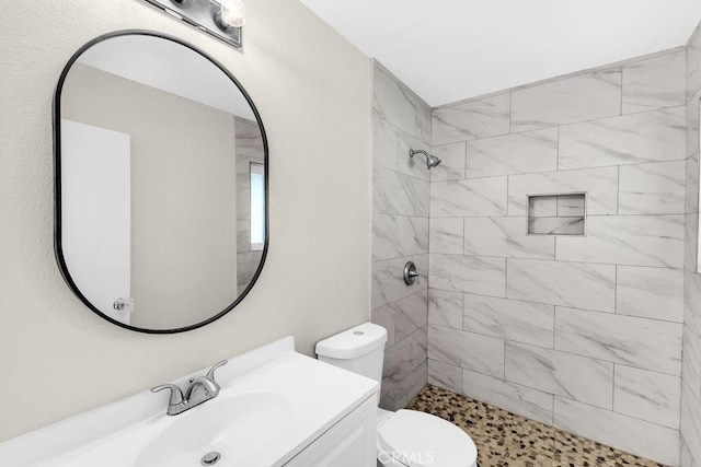 bathroom with toilet, tiled shower, and vanity
