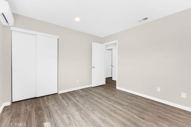 unfurnished bedroom with baseboards, a wall unit AC, visible vents, and wood finished floors
