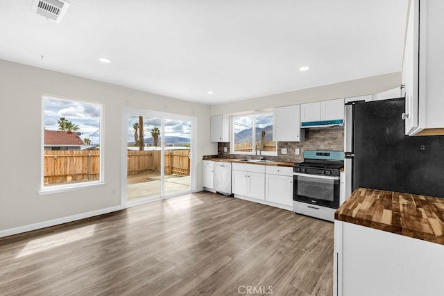 kitchen with under cabinet range hood, wooden counters, visible vents, backsplash, and appliances with stainless steel finishes