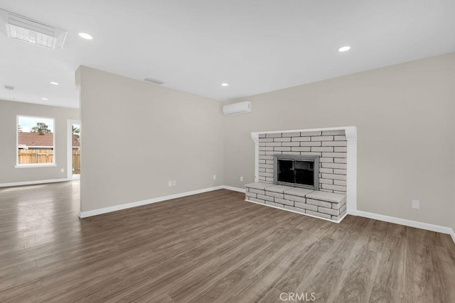 unfurnished living room with a wall mounted air conditioner, baseboards, visible vents, wood finished floors, and a fireplace