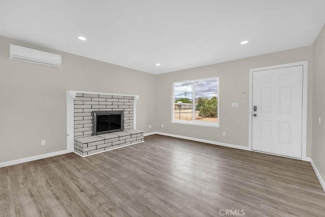 unfurnished living room with recessed lighting, a wall mounted AC, baseboards, a brick fireplace, and wood finished floors