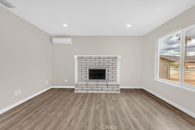 unfurnished living room with an AC wall unit, baseboards, visible vents, wood finished floors, and a fireplace