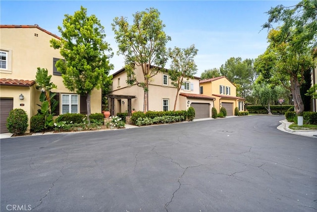 exterior space featuring an attached garage, a tiled roof, stucco siding, and aphalt driveway