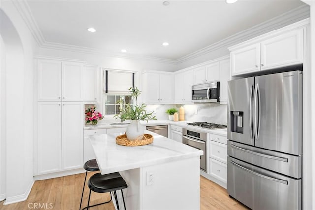 kitchen with light wood finished floors, a center island, a kitchen bar, stainless steel appliances, and white cabinets