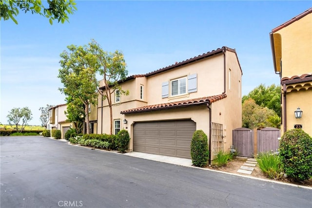 mediterranean / spanish-style house featuring stucco siding, a tile roof, an attached garage, and a gate