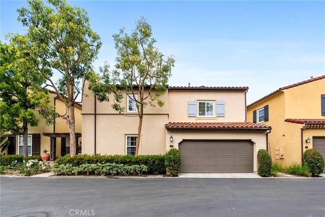 mediterranean / spanish house with driveway, stucco siding, a tiled roof, and a garage