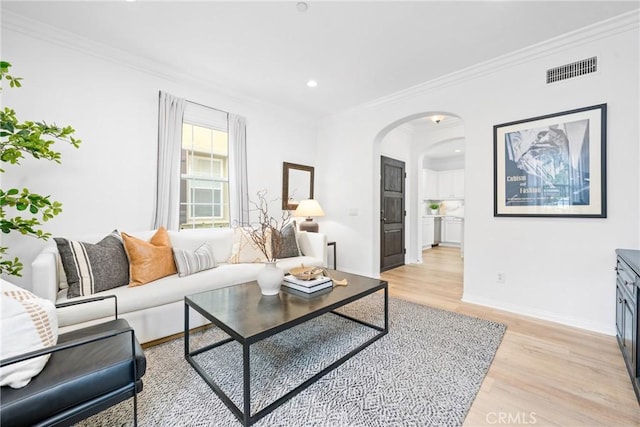 living room featuring arched walkways, crown molding, light wood-style flooring, and visible vents
