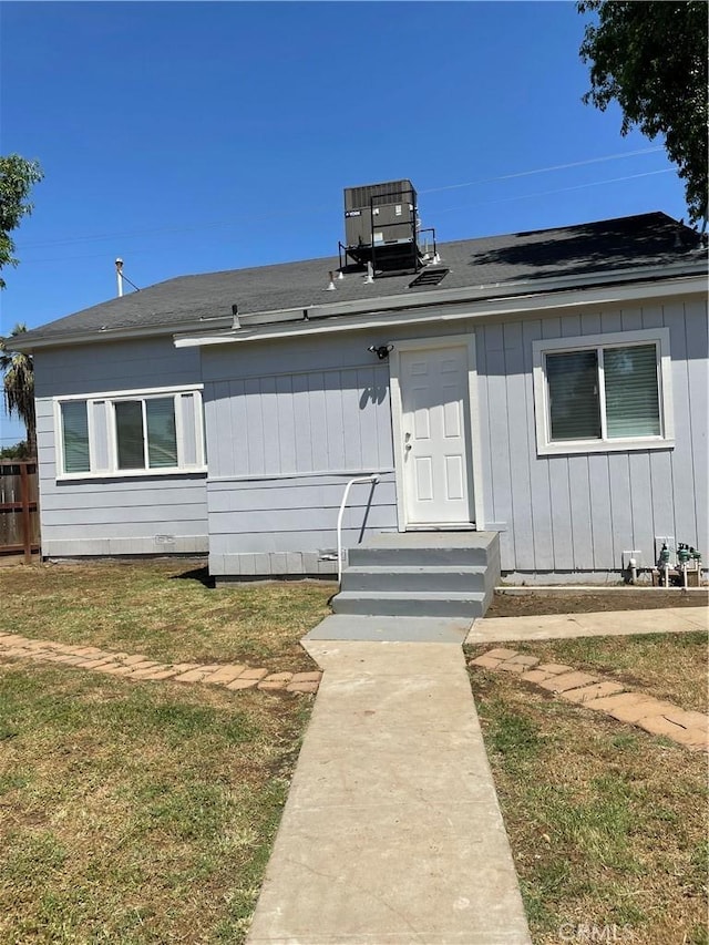 view of front of property featuring roof with shingles, central AC, and a front yard