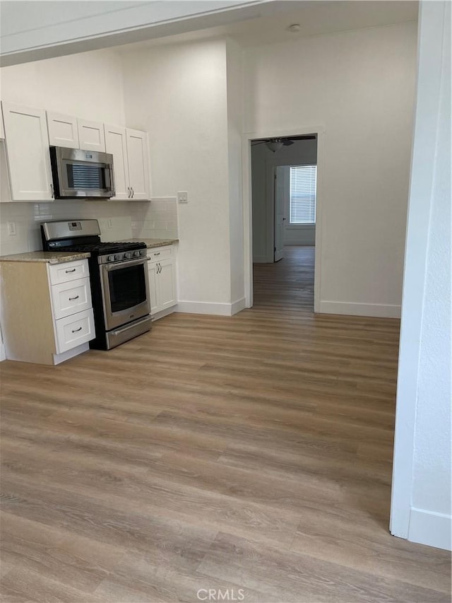 kitchen featuring light wood finished floors, baseboards, white cabinets, and appliances with stainless steel finishes