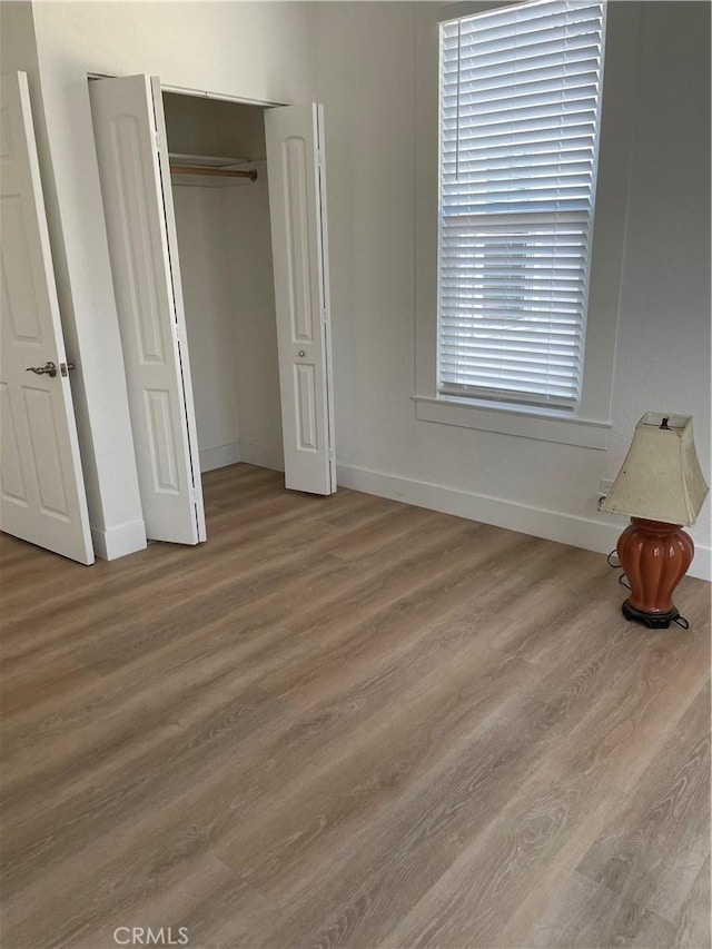 unfurnished bedroom with a closet, wood finished floors, and baseboards