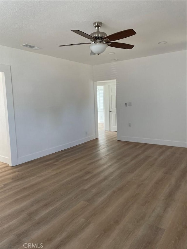empty room with visible vents, wood finished floors, baseboards, and ceiling fan