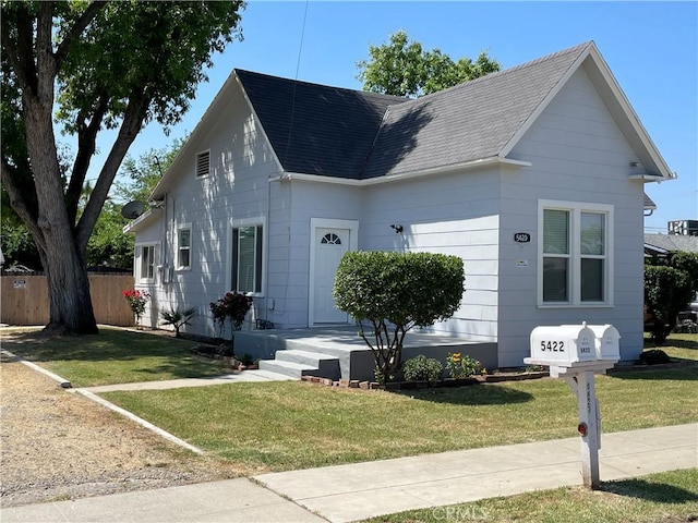 view of front of property featuring roof with shingles, fence, and a front yard