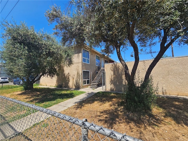 view of front of property with stucco siding, fence, a front yard, and stairs